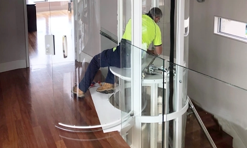 An elevator technician in process of installing a white framed Savaria Vuelift Mini winding drum elevator.