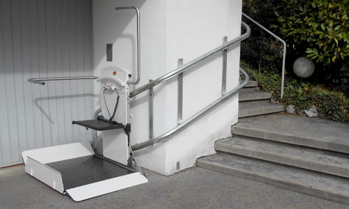 A custom twin rail incline platform lift installed along the wall of an outdoor stone staircase.