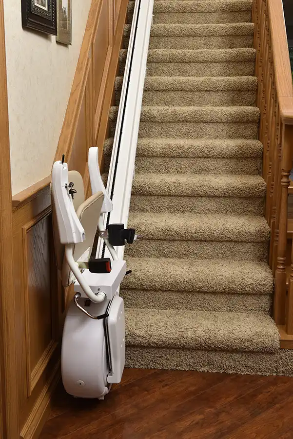 Savaria straight chair lift folded at the base of a staircase with the seat and footrest raised