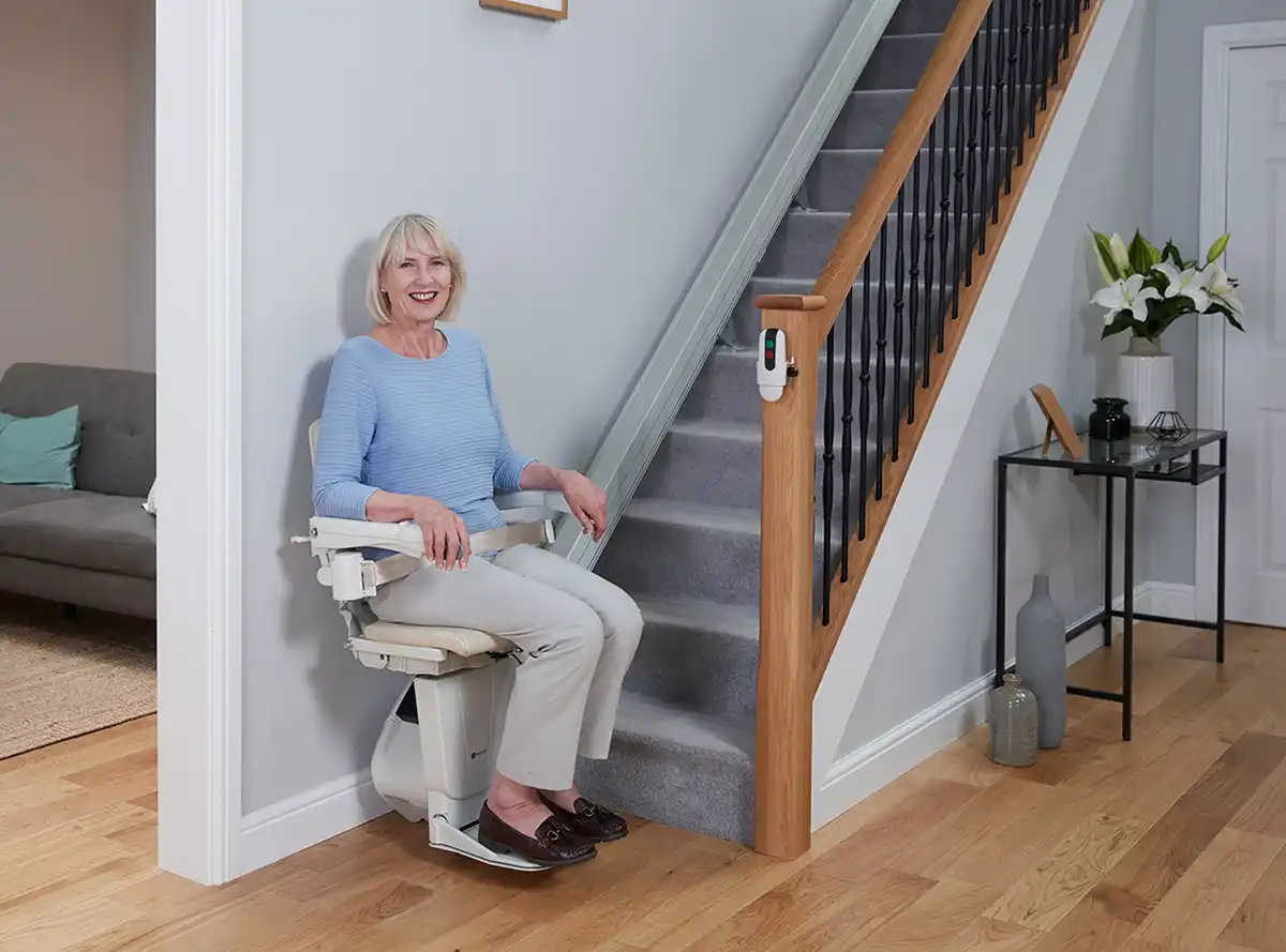 Woman seated on a Savaria Handicare 1100 stairlift at the bottom landing | stairway glide chairlift price and cost
