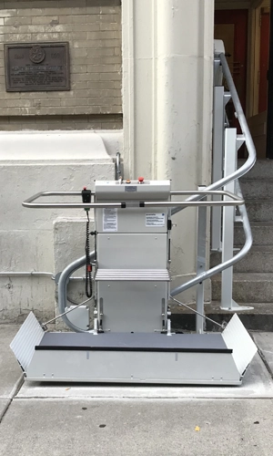 Outdoor inclined platform lift installed beside a staircase, shown in the lowered position.