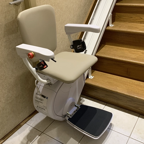 Indoor straight stair lift with beige cushioned seat and armrests installed along a straight rail.