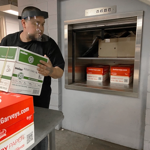 Worker operating a material lift to transport office supplies and boxes of paper, ensuring safe and efficient handling.