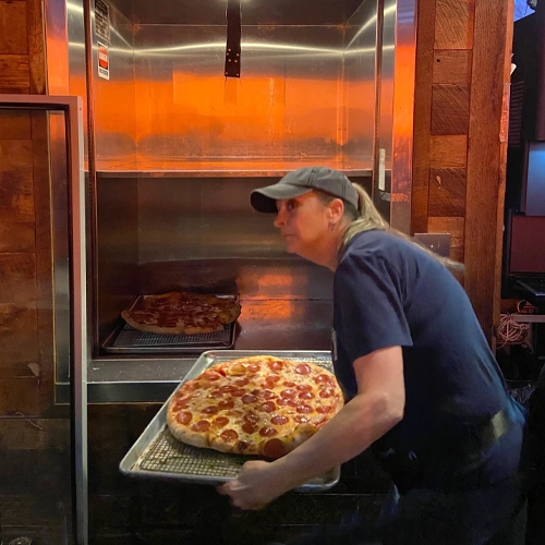 Pizza chef transporting two pepperoni pizzas to the dining area using a material lift, ensuring safe and efficient delivery.