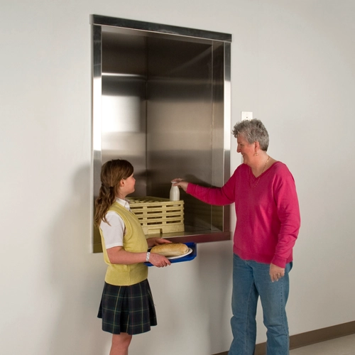A teacher and student using a material lift to transport food and drinks to another floor, demonstrating safe handling in a school setting.