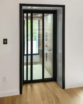 Auto‑slim elevator doors with narrow glass panels and a black frame, shown partially open within a modern home interior.