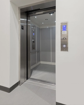 Modern commercial elevator with stainless steel door frames, bright interior lighting, and smooth gray wall panels, shown with the cab open at the fourth floor.