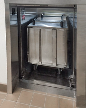 Stainless steel material lift with a wheeled metal cart positioned inside the open lift compartment.
