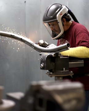 Grinding sparks flying from a curved stairlift rail held in a vise as it is shaped and finished with a power tool.