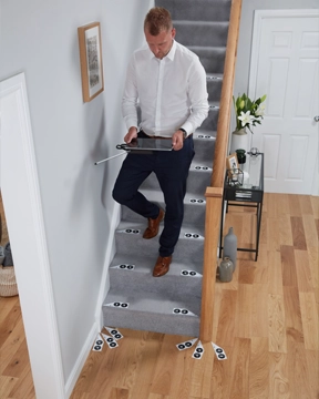 Person using photo‑imaging equipment to scan and measure a carpeted staircase marked with reference targets for stairlift planning.