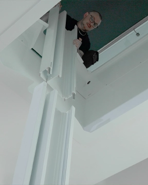 Installation in progress for a through‑the‑floor lift, showing a partially assembled vertical rail structure being positioned from the upper level.