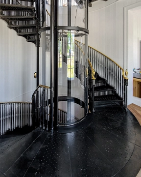 Glass home elevator surrounded by a black spiral staircase with gold handrail accents in a modern interior.