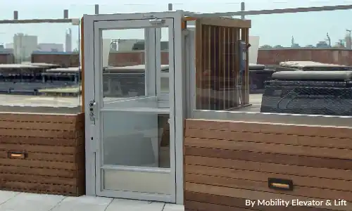 Outdoor rooftop vertical platform lift with glass door enclosure, providing wheelchair‑accessible access to a residential terrace or rooftop patio.