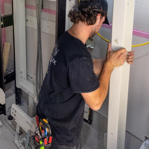Elevator technician installing and securing vertical structural components inside a residential home elevator shaft during lift installation.