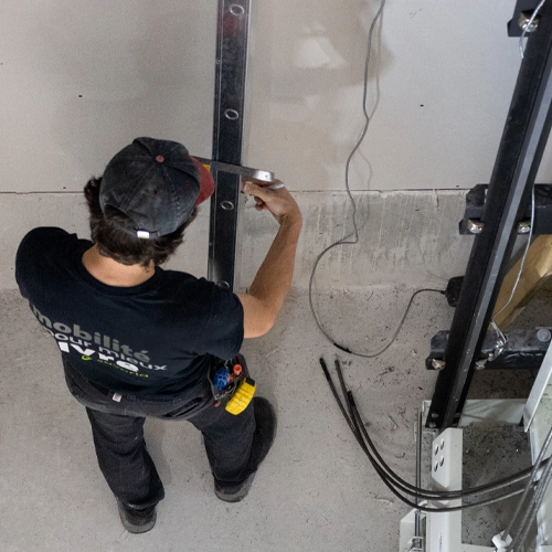 Elevator technician measuring and aligning vertical guide rail inside a residential home elevator shaft during installation.