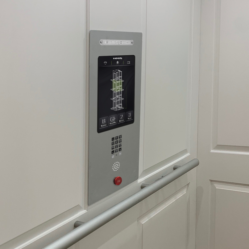 Stainless steel residential elevator control panel with digital floor display, illuminated buttons, emergency stop, speaker grille, and horizontal handrail mounted on a white cabin wall.
