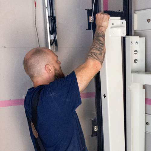 Elevator technician installing vertical guide rail components inside a residential lift shaft during home elevator installation.