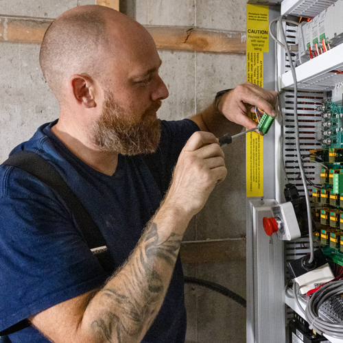 Elevator service technician performing electrical maintenance on a residential elevator control cabinet, adjusting wiring and components for safe and reliable lift operation.