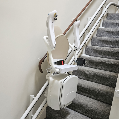 Indoor stair lift chair with beige seat and armrIndoor stair lift chair with beige seat and armrests installed along a straight rail.ests installed along a straight rail.