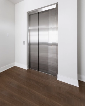 Closed stainless steel elevator doors set within a white wall and dark wood flooring