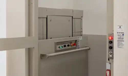 Savaria MultiLift vertical platform lift with interior control panel, safety handrail, emergency stop button, and durable gray enclosure for wheelchair accessibility.